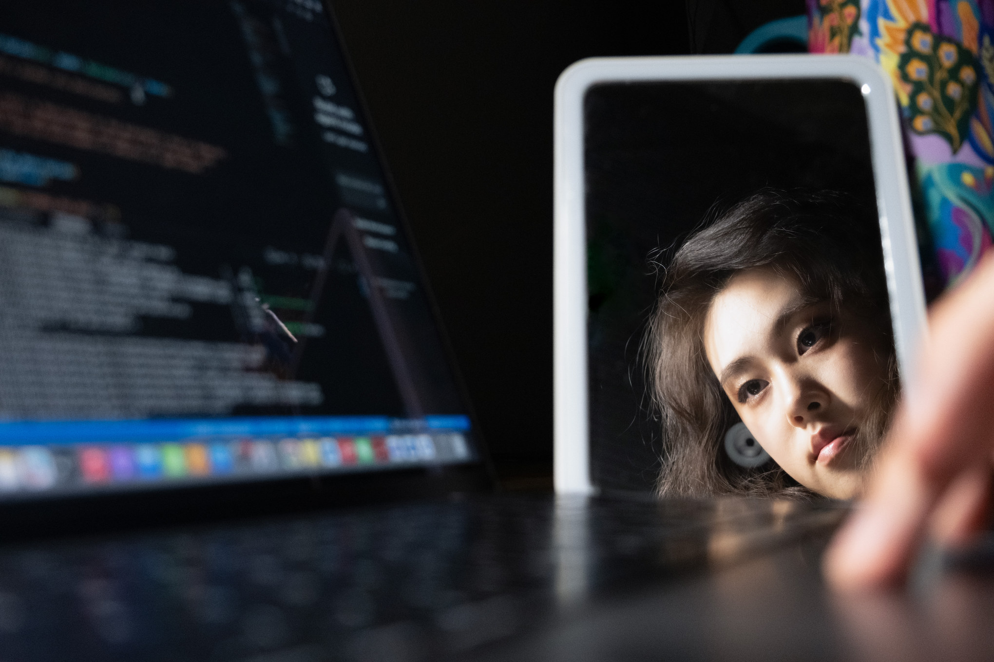 Chenchen Zheng reflected in a mirror beside a laptop displaying code.