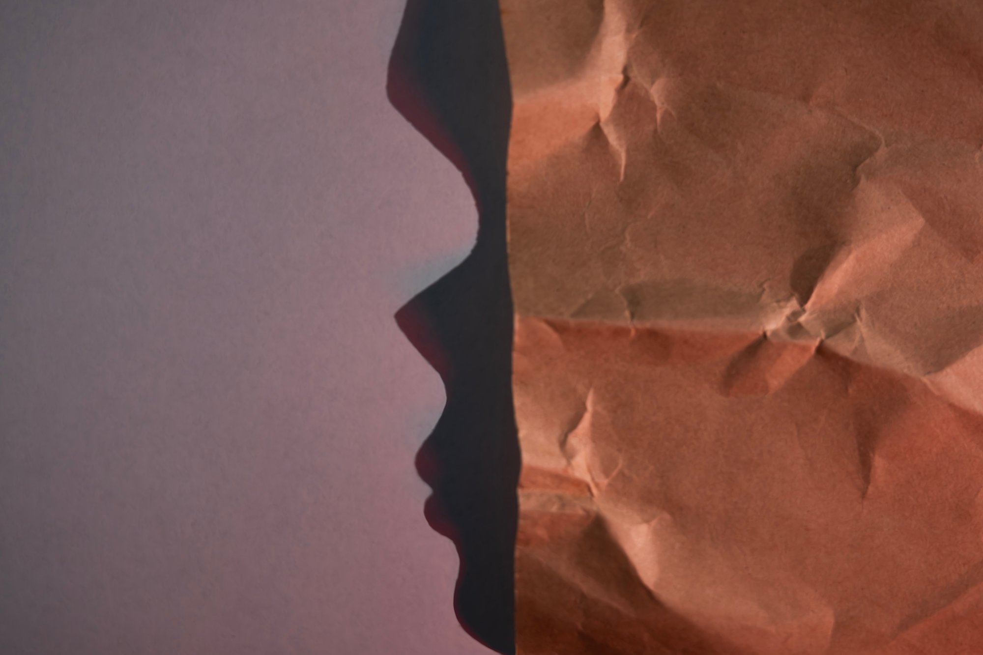 Directional light on crumpled paper creates a dark edge resembling a face in profile against a pale field.